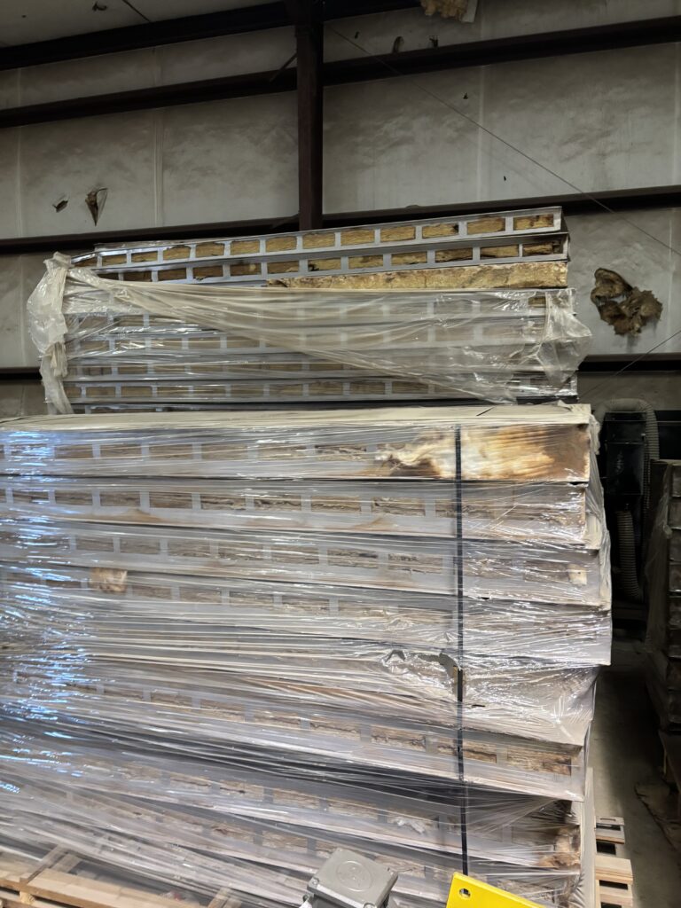 Stacks of wrapped pallets in a warehouse, metal frames exposed and plastic sheeting covering the loads.