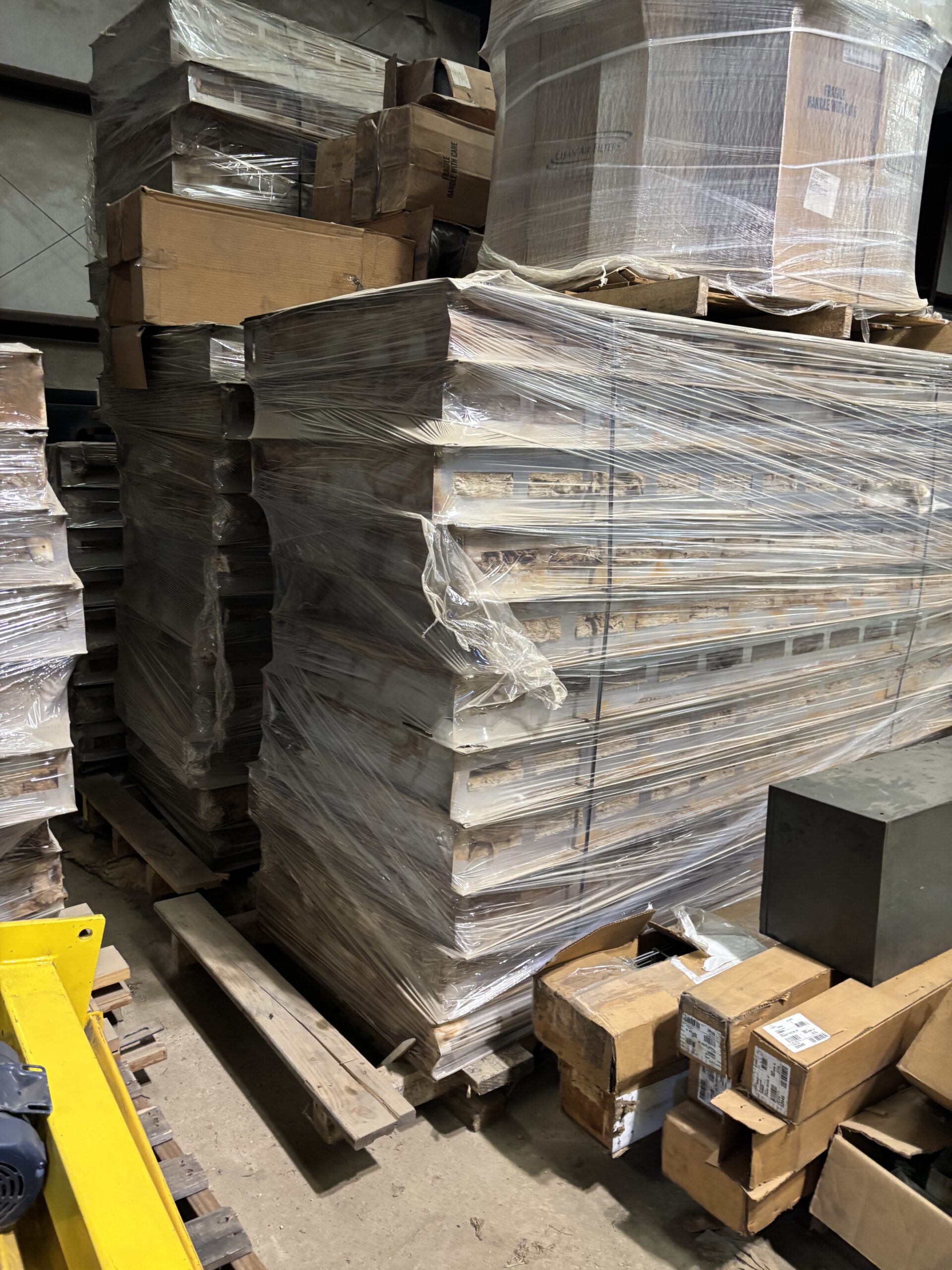 Pallets wrapped in plastic and stacked cardboard boxes in a dim warehouse storage area.