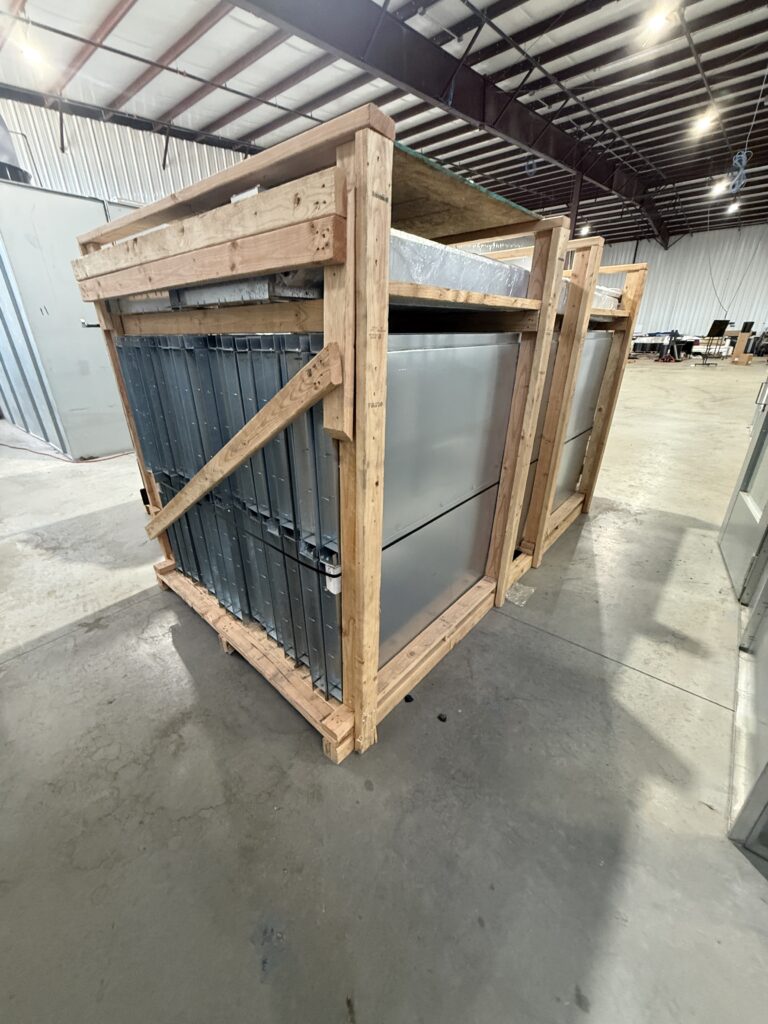 Large wooden crate holding stacked metal panels in an industrial warehouse.