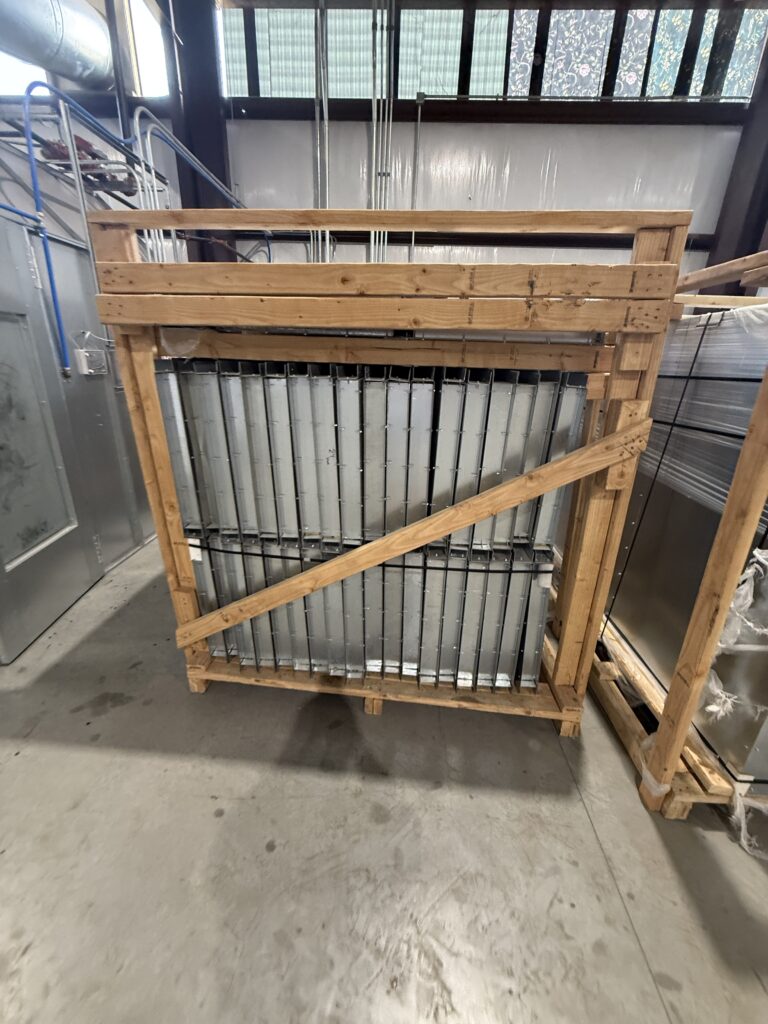 Stack of metal louvered panels secured in a wooden shipping crate in a warehouse setting