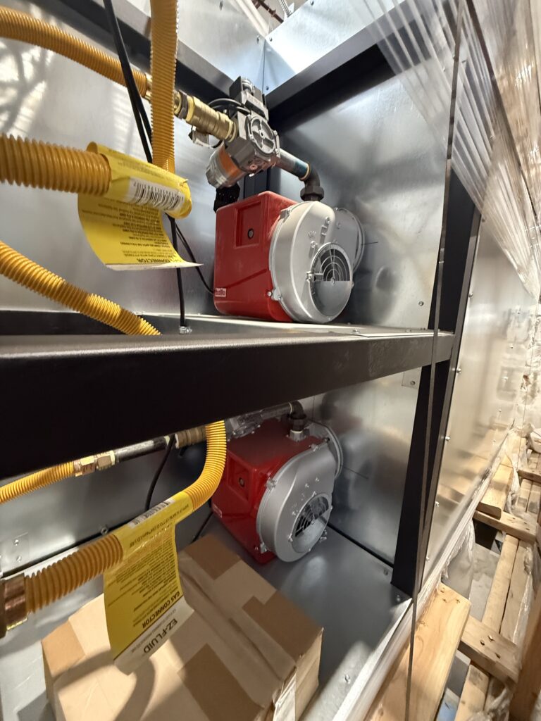 Industrial blower/pump unit with red motor housing and gray fan cover inside a metal enclosure, with yellow electrical conduits nearby.