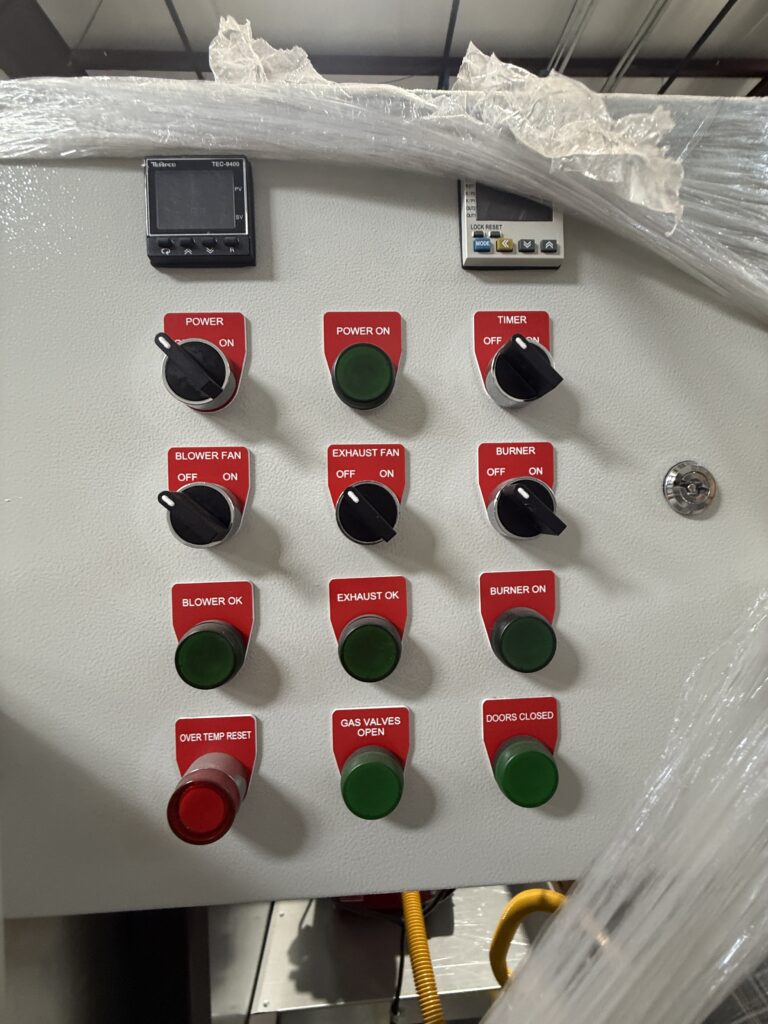 Industrial control panel with red labeled switches (POWER ON, BLOWER OK, EXHAUST OK) and green indicator buttons; plastic wrap partially covering top.