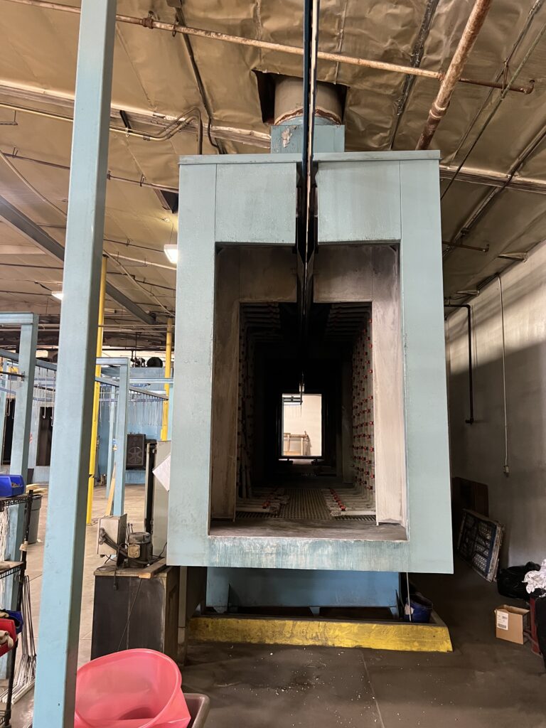 Industrial machinery: a large blue steel frame with a narrow central passage and conveyor/roller system in a workshop.