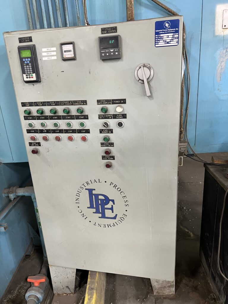 Industrial control panel with numerous green indicator lights and labeled push buttons in an industrial setting.