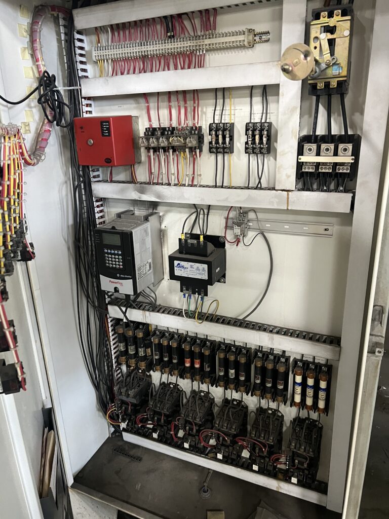 Electrical control panel with numerous red, black, and yellow wires and terminal blocks inside a metal cabinet.