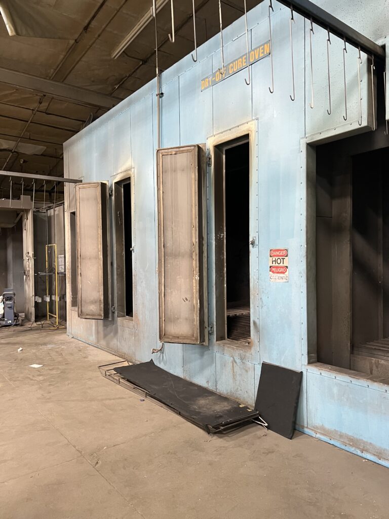 Blue industrial curing oven with multiple open doors and hanging metal hooks inside a warehouse setting.